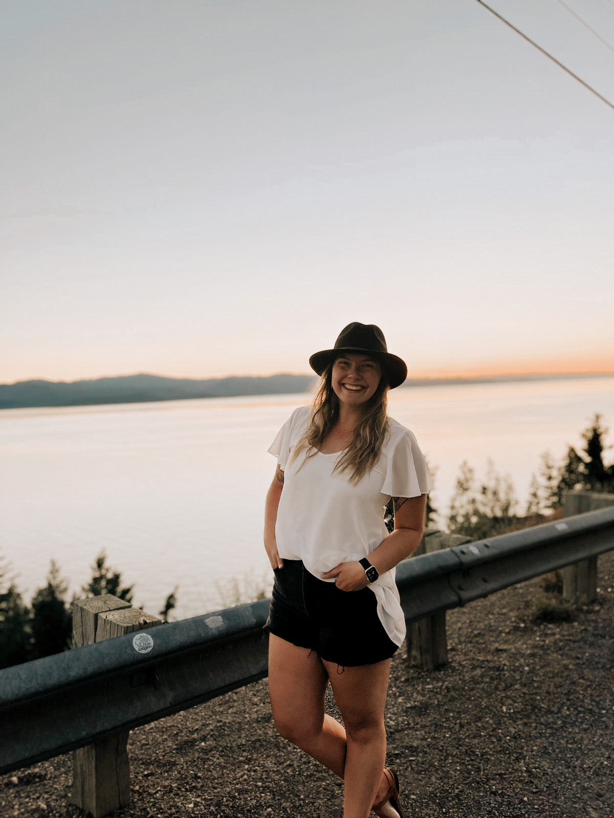 hannah zuraff posing next to a guardrail on a road alongside a large lake